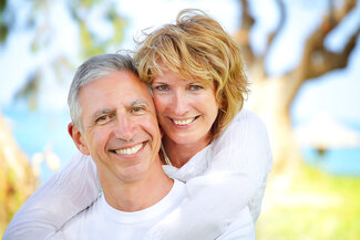 mature couple smiling with nice teeth, outdoors near water and trees, Sarasota, FL veneers